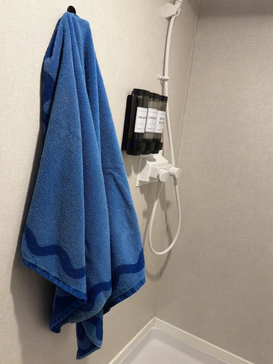 Compact RV rental shower with blue towel, wall-mounted toiletries (shampoo, conditioner, body wash), and shower head.. Coleman 23B Keystone 2025