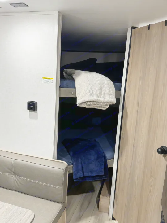 Interior of an RV rental featuring cozy bunk beds with blankets, a dinette seat, and a thermostat on the wall.. Coleman 23B Keystone 2025
