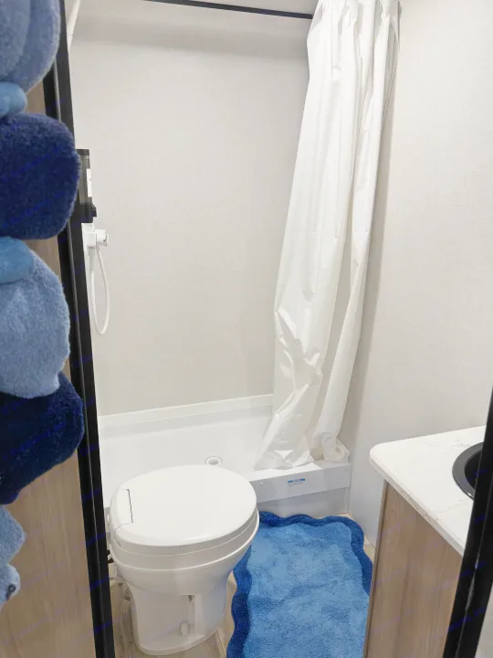 Compact RV rental bathroom features a toilet, shower with curtain, and vanity. Practical for your travel needs.. Coleman 23B Keystone 2025