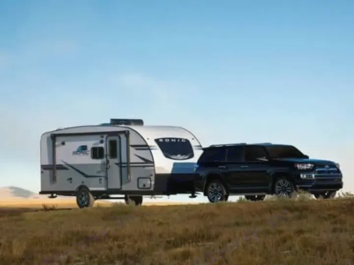 Explore with an RV rental! A black SUV tows a modern travel trailer on a grassy hill under a clear sky, ideal for outdoor trips.. Sonic Lite 2021