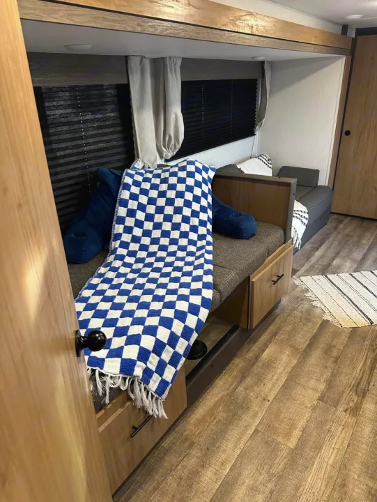 Inside an rv rental: a cozy bunk area with a blue/white checkered blanket, storage, seating, and wood floors.. Forest River Campsite reserve 25MW 2024