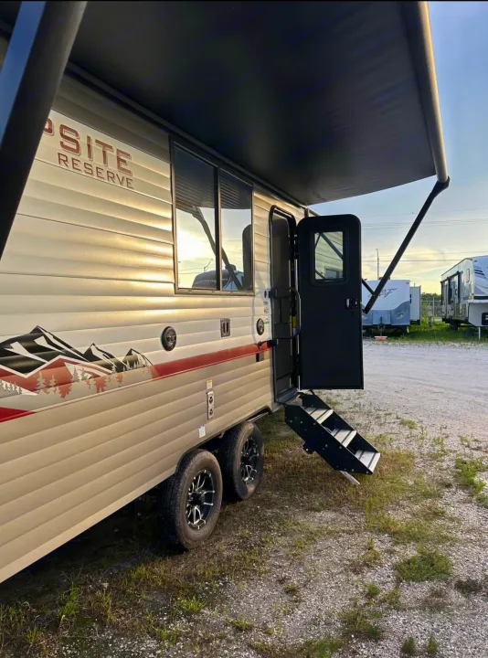Spacious tan rv rental with extended awning, open door, entry steps, and mountain-themed graphics, parked in an outdoor lot.. Forest River Campsite reserve 25MW 2024