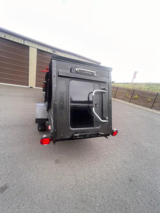Black compact RV rental, rear view with door, window, red tail lights. Parked near storage units, a "Wrong Way" sign visible.. Custom Squaredrop Trailer 2020