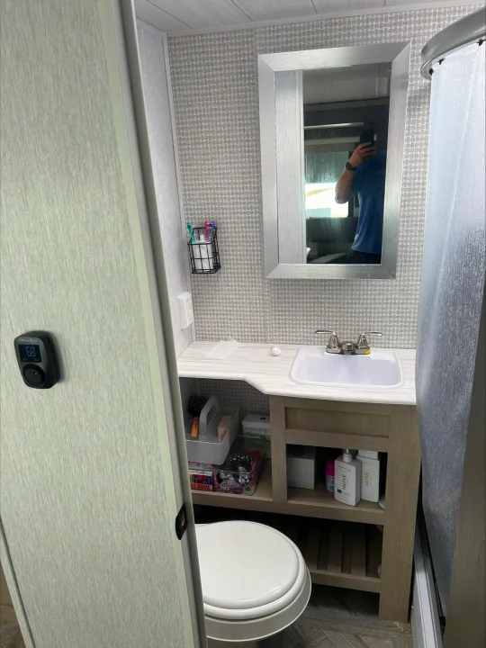 Compact RV rental bathroom with a sink, mirror, toilet, and storage under the vanity. Temperature is set to 68.. Forest River Wildwood 2024