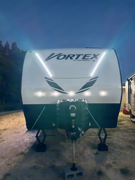 Experience camping with this Vortex RV rental! Front view of a white travel trailer at night, illuminated by bright V-shaped LED lights.. Genesis Supreme Rv Genesis Supreme 2025