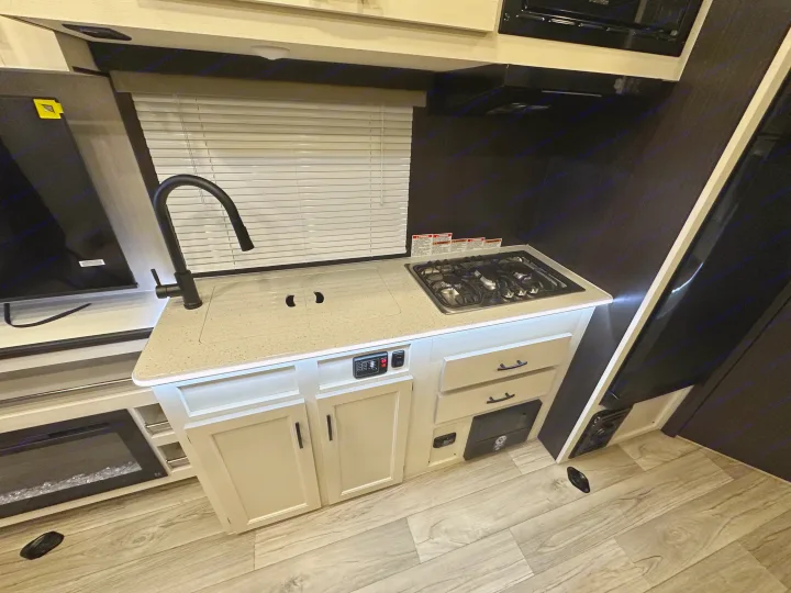 RV rental kitchen: modern light countertop, covered sink, three-burner stove, black faucet, cabinets, wood-look floor.. Genesis Supreme Rv Genesis Supreme 2025