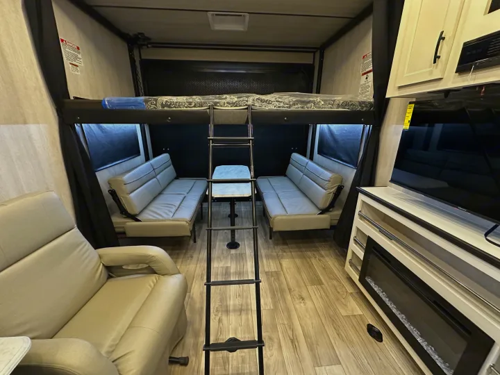 Cozy rv rental interior featuring a bunk bed with ladder, convertible sofas, recliner, and electric fireplace.. Genesis Supreme Rv Genesis Supreme 2025