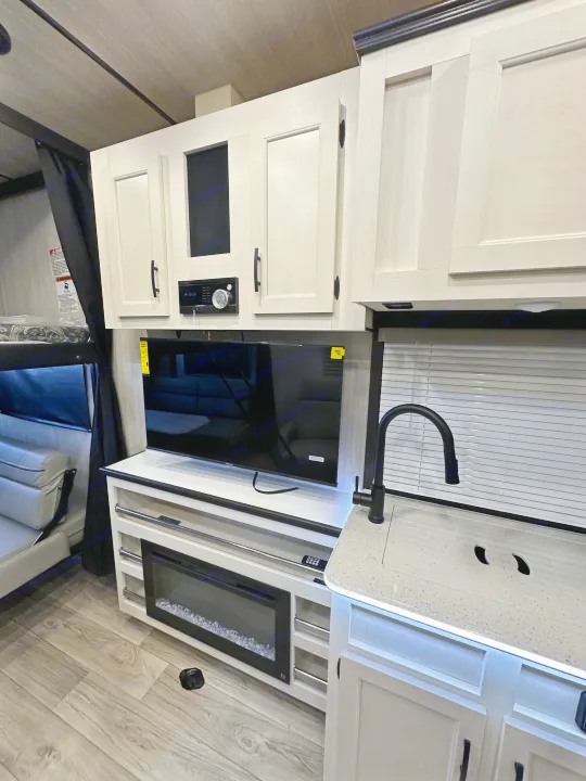 Modern RV rental interior: kitchen sink, TV, fireplace, and bunk beds in a compact, light-toned space.. Genesis Supreme Rv Genesis Supreme 2025