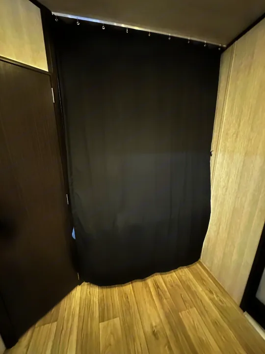 RV rental interior: A black privacy curtain hangs from a track across the room, with a light wood-look floor and a dark door on the left.. Genesis Supreme Rv Genesis Supreme 2025