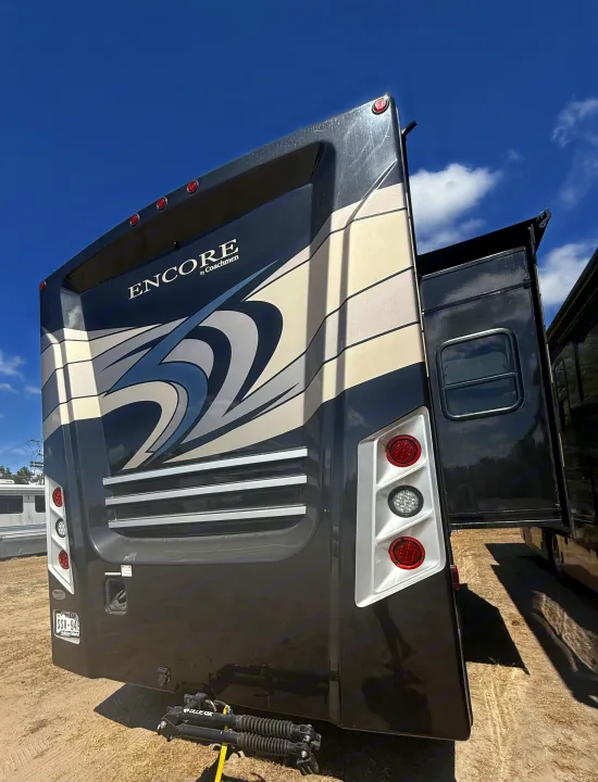 Rear of a dark ENCORE by Coachmen RV rental, featuring an extended slide-out, taillights, and towing hitch under a blue sky.. Coachmen Encore 2022