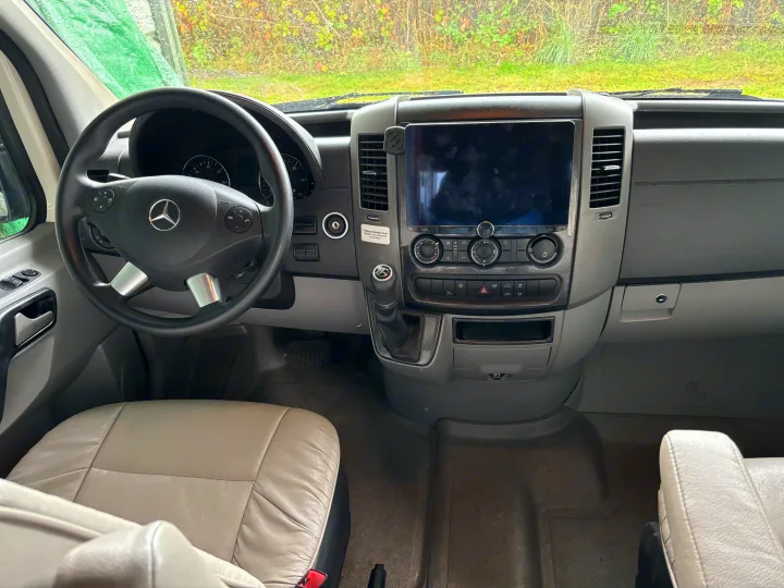 Inside an RV rental: the driver's view of the dashboard with a Mercedes steering wheel, large screen, and various controls.. Pleasure-Way Pleasure-Way Class B 2016