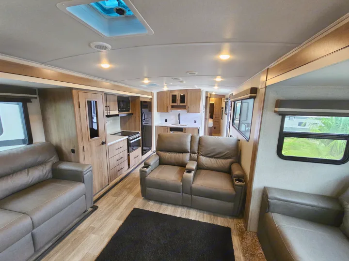 Spacious, modern RV rental interior featuring a full kitchen, comfortable living area with recliners and a sofa.. Grand Design Imagine 2024
