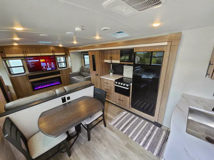 Spacious rv rental living area: modern kitchen with full appliances, dining booth, and living room featuring a TV and fireplace.. Grand Design Imagine 2024