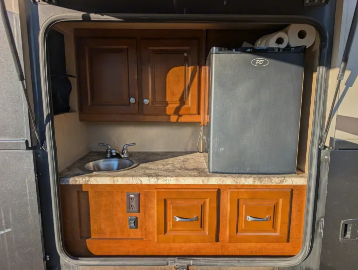 This RV rental outdoor kitchen features a compact sink, mini-fridge, and storage cabinets, ideal for convenient camping.. Thor Miramar 2015