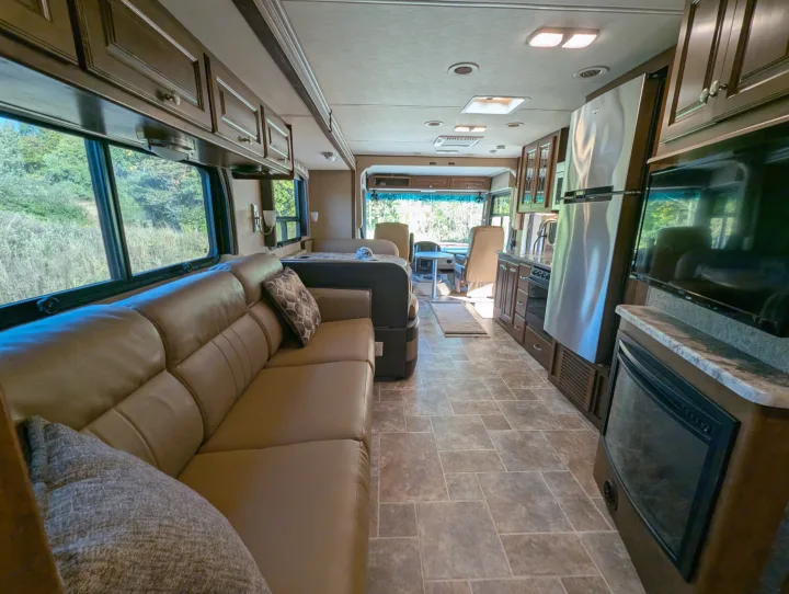 Spacious RV rental interior with a cozy brown leather sofa, full kitchen, dining area, and driver's cabin, offering scenic views.. Thor Miramar 2015