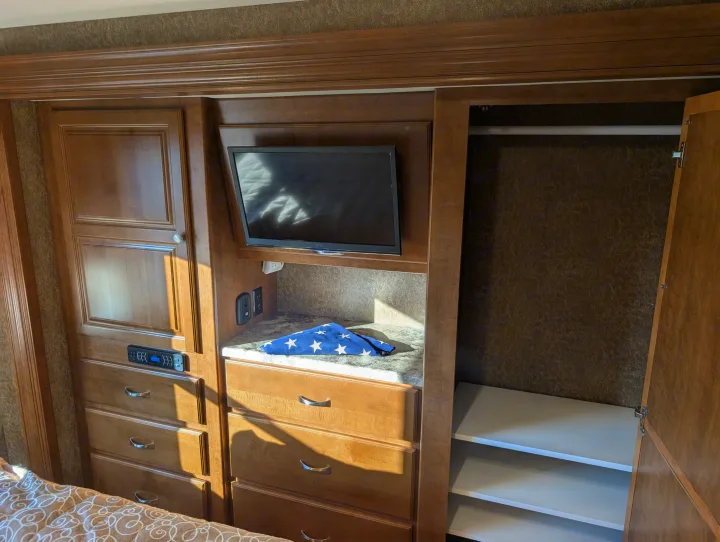 RV rental interior: wooden unit with TV, storage drawers, open closet with shelves, and a folded flag on the counter.. Thor Miramar 2015