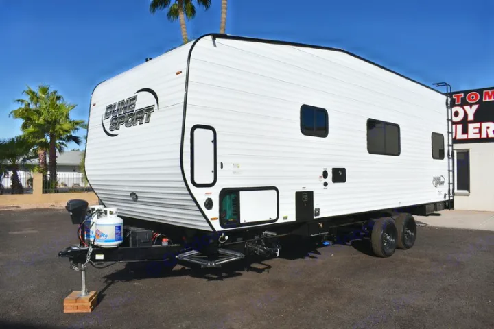 Modern white Dune Sport toy hauler, available for RV rental, featuring black trim and visible propane tanks under a blue sky.. Dune Sport Dynamite 2023
