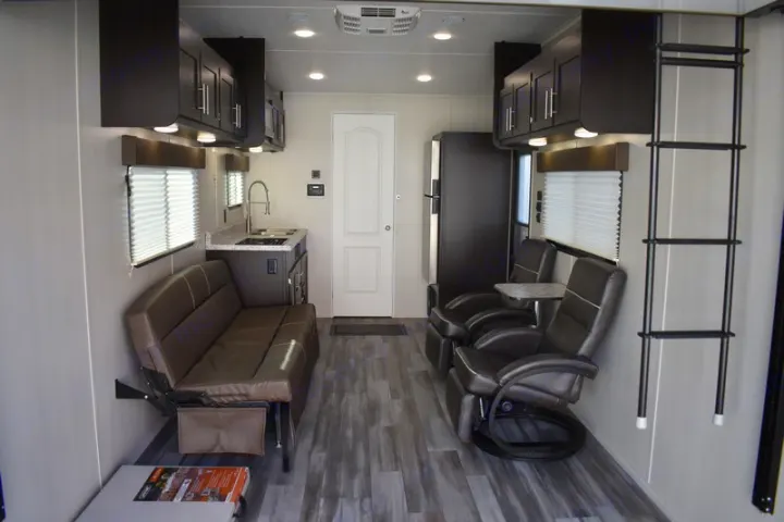 This RV rental interior features a compact kitchen, comfortable living area with sofa and recliners, and wood-look flooring.. Dune Sport Dynamite 2023