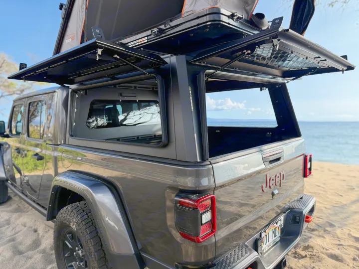 Overland in this dark gray Jeep Gladiator RV rental, featuring a rooftop tent & open truck bed camper by the ocean.. Jeep Gladiator 2022