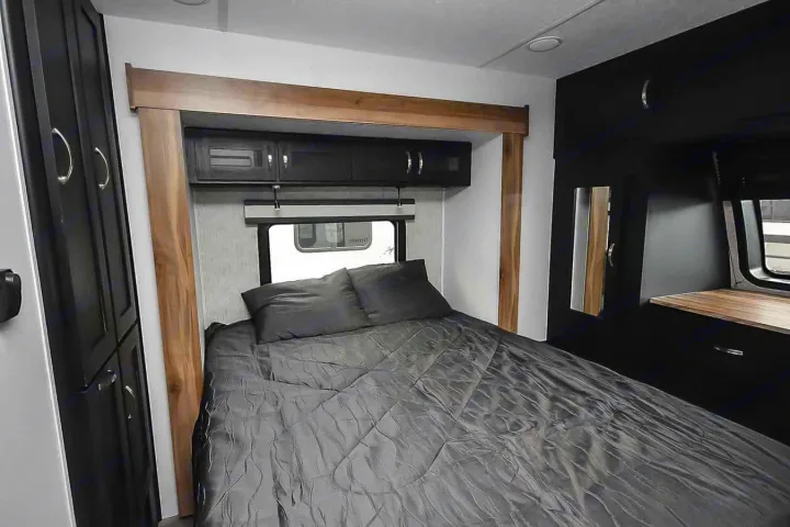 This modern RV rental bedroom features a comfy bed with dark bedding, overhead cabinets, and wood accents, creating a stylish interior.. Coachmen Coachmen Freedom Express Liberty Edition (324RLDSLE) 2022