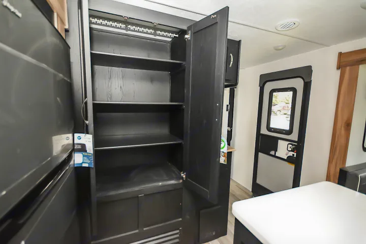 Inside an RV rental: a dark, open pantry with multiple shelves & a glimpse of the entry door & outside.. Coachmen Coachmen Freedom Express Liberty Edition (324RLDSLE) 2022
