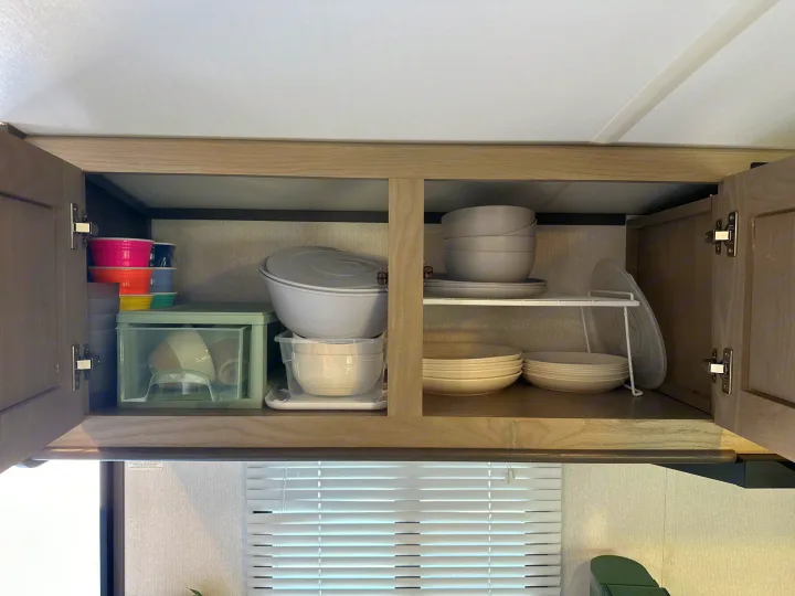 Organized dishes and cups in an open overhead cabinet of an RV rental, showcasing practical kitchen storage.. Cruiser RV Shadow Cruiser 2021