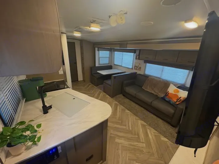Modern RV rental interior: open layout with kitchen counter/sink, sofa with throw pillow, and dinette. Features light wood-look flooring.. Cruiser RV Shadow Cruiser 2021