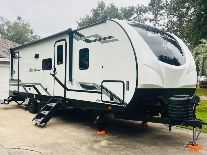 An Eddie Bauer travel trailer RV rental is parked on a driveway with its steps and stabilizers extended, ready for your next adventure.. Heartland RVs 265BH-L 2024