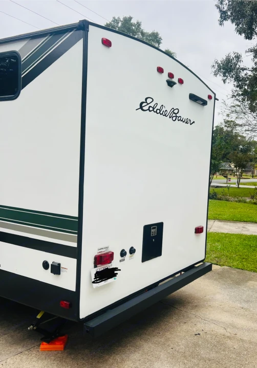 Rear of a white Eddie Bauer RV rental with green stripes, showing taillights, utility panel, and Georgia plate. Parked on concrete.. Heartland RVs 265BH-L 2024