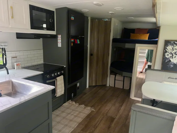 A modern rv rental interior showcasing a dark kitchen with white counters, subway tile backsplash, bunk beds, and a dinette.. Heartland RVs 265BH-L 2024