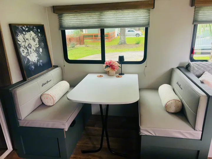 Inside a cozy RV rental: a bright dinette with light grey seating, a white table, flowers, art, and scenic window views.. Heartland RVs 265BH-L 2024