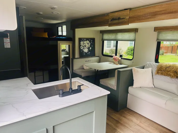 Step inside this RV rental! Features a light green kitchen, dining booth, sofa, and bunk beds. Modern and cozy interior design.. Heartland RVs 265BH-L 2024