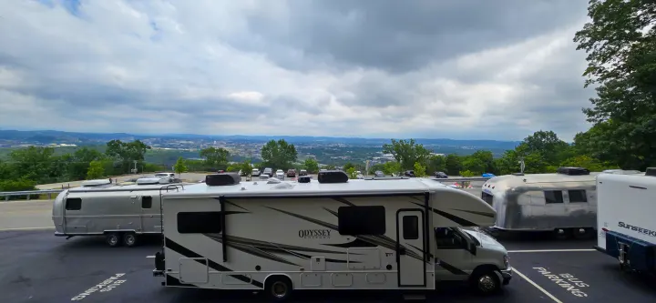 RV rentals: an Odyssey motorhome, a silver travel trailer, and a Sunseeker RV parked overlooking a scenic city view.. Entegra Coach Odyssey 2024