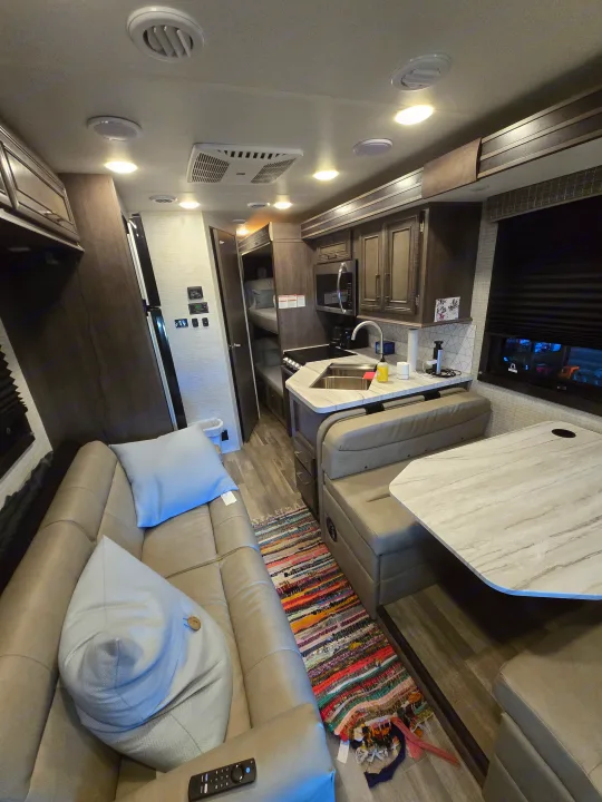 Modern RV rental interior featuring a full kitchen, comfortable dining booth, couch, and cozy bunk beds. Ideal for family adventures.. Entegra Coach Odyssey 2024