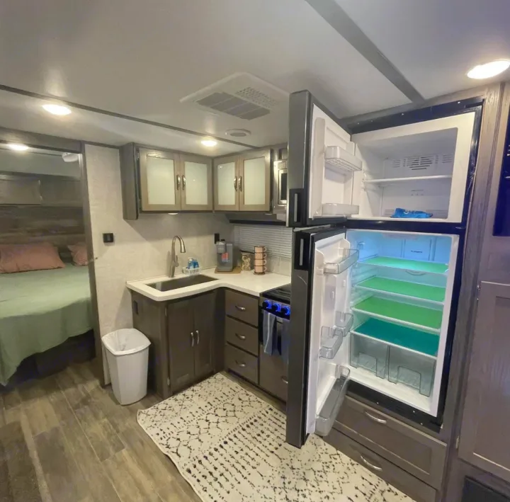 Compact RV rental interior showcasing a kitchen with an open fridge (green liners), sink, and a comfortable bedroom.. Gulf Stream Envision 2023