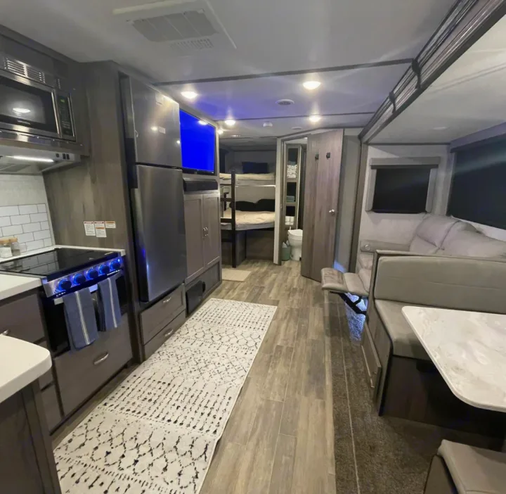 Modern RV rental interior with a fully equipped kitchen, dining area, cozy sofa, and bunk beds for family comfort.. Gulf Stream Envision 2023
