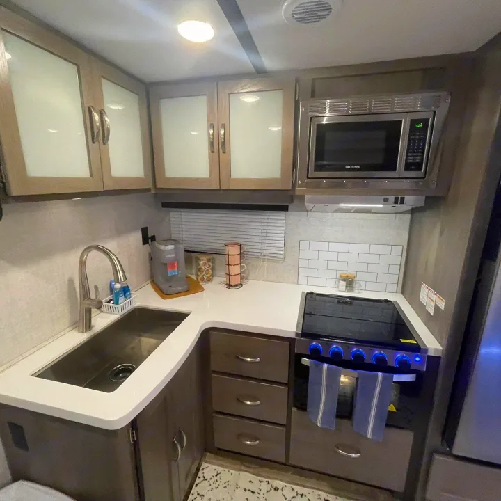 Modern RV rental kitchen showcasing a stainless steel sink, overhead microwave, and stovetop with oven below for travelers.. Gulf Stream Envision 2023
