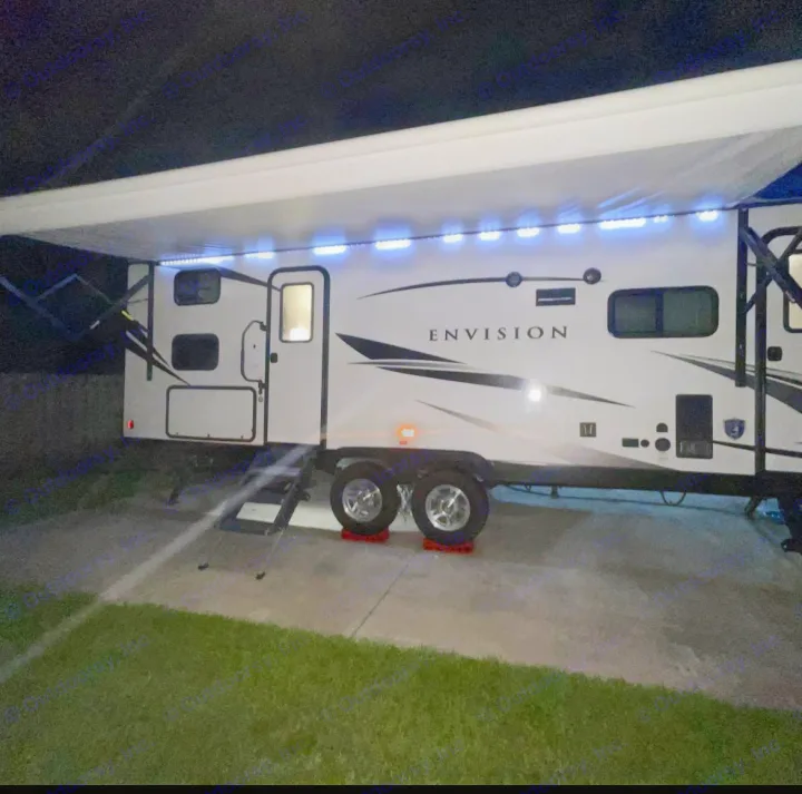 Bright RV rental illuminated by LED awning lights at night, parked on a paved pad with steps down to the grass. Perfect for a camping adventure.. Gulf Stream Envision 2023