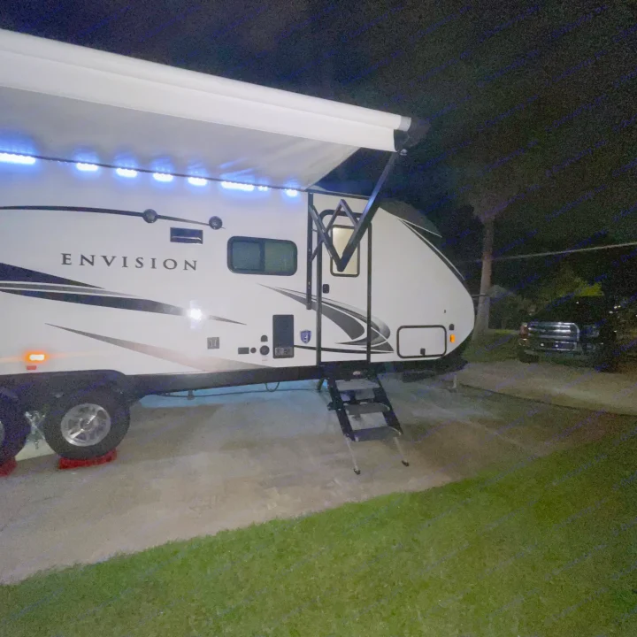 Enjoy an RV rental: A white Envision travel trailer at night, with a lit awning extended, parked on pavement with stairs.. Gulf Stream Envision 2023