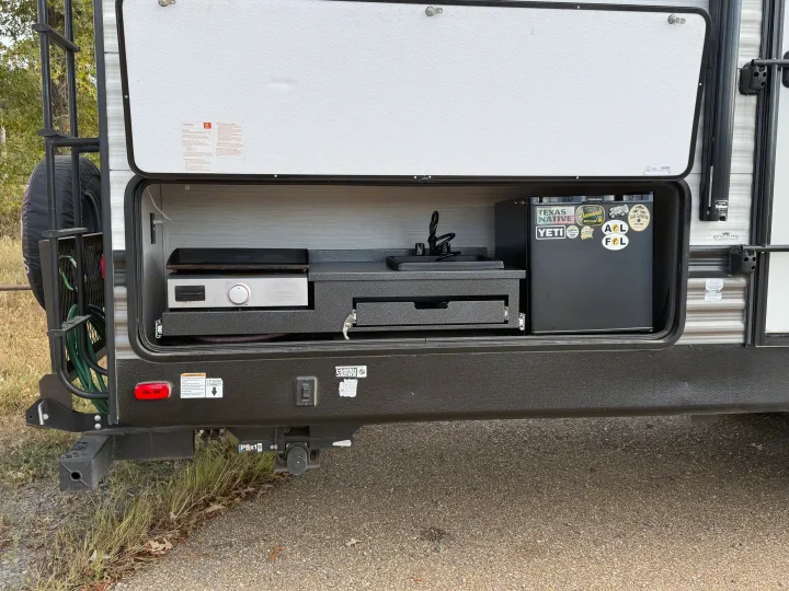 This rv rental offers an outdoor pull-out kitchen with a griddle, sink, and mini-fridge adorned with travel stickers.. Forest River Palomino Puma 2021