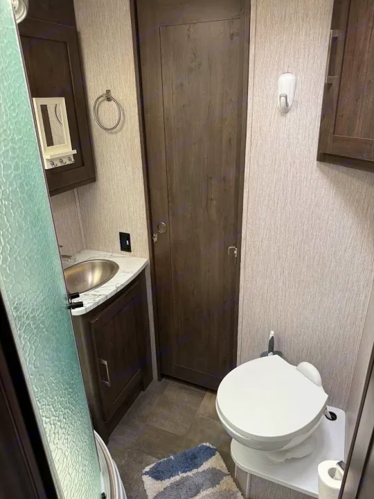 Inside an RV rental bathroom: compact shower, sink vanity, and toilet. Features wood cabinetry and light walls.. Coachmen Pursuit 2022