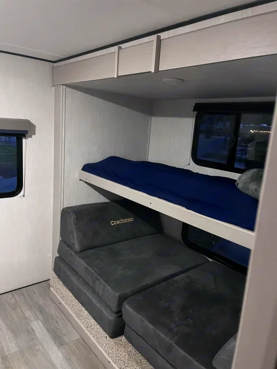 RV rental interior: bunk beds with blue bedding, 'Coachmen' modular seating, and windows. Comfortable sleeping/living space.. Coachmen Apex 300 BHS 2025
