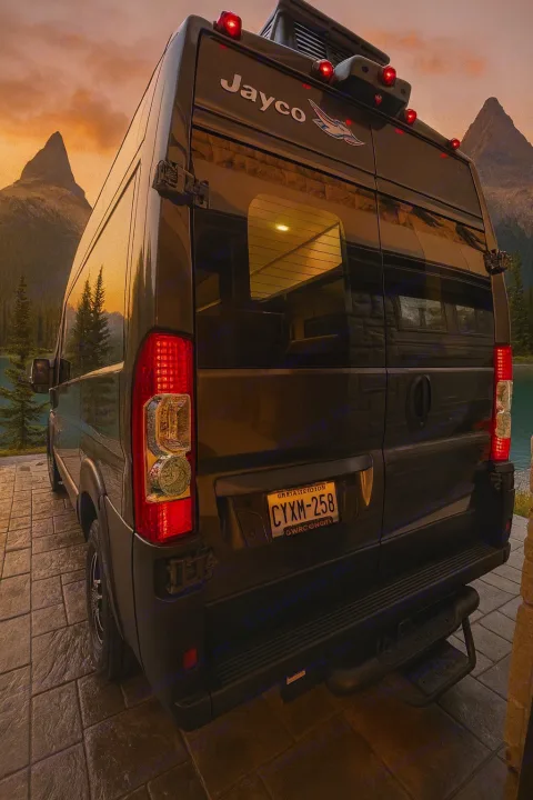 Rear view of a dark Jayco RV rental camper van at sunset, parked lakeside with mountains in the background.. Jayco Swift 2023