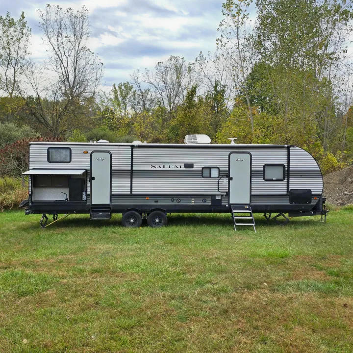 This RV rental is a grey and white Salem travel trailer with an outdoor kitchen, parked on grass surrounded by trees.. Forest River Salem 2019