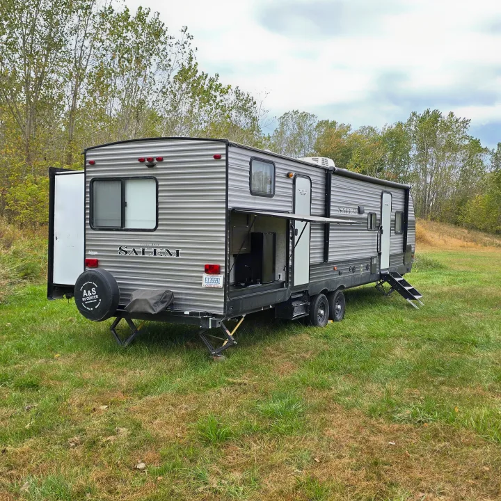 A Salem travel trailer RV rental from A&S RV Center, featuring an outdoor kitchen, set up in a lush, grassy field.. Forest River Salem 2019