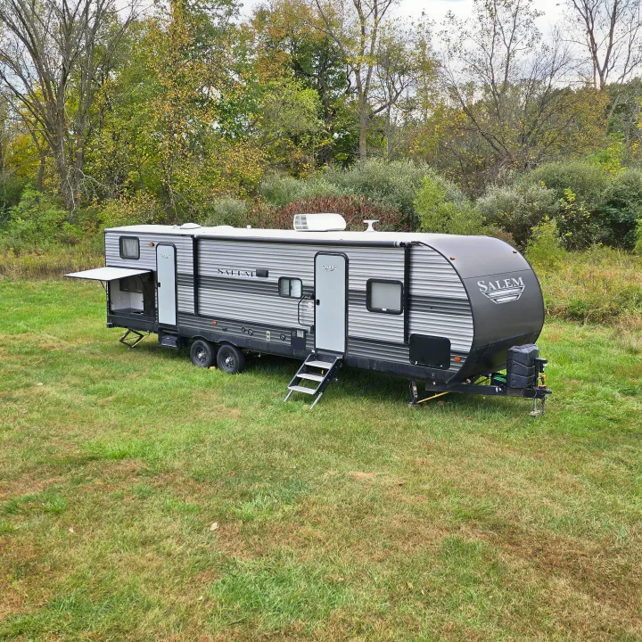 Explore nature with this Salem RV rental, a travel trailer setup in a scenic grassy field surrounded by trees.. Forest River Salem 2019