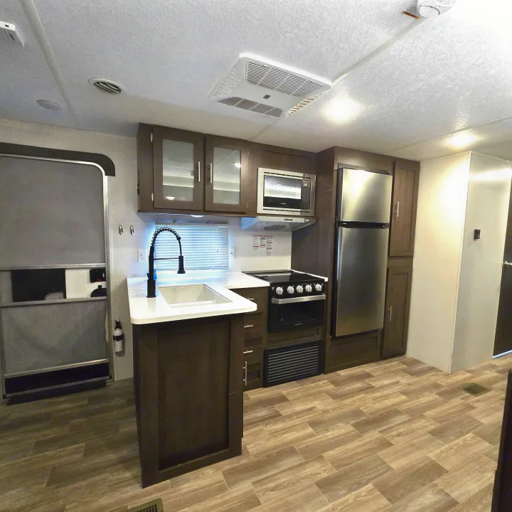 Inside a modern RV rental: spacious kitchen with island sink, stainless appliances, dark cabinets, and wood-look flooring.. Forest River Salem 2019