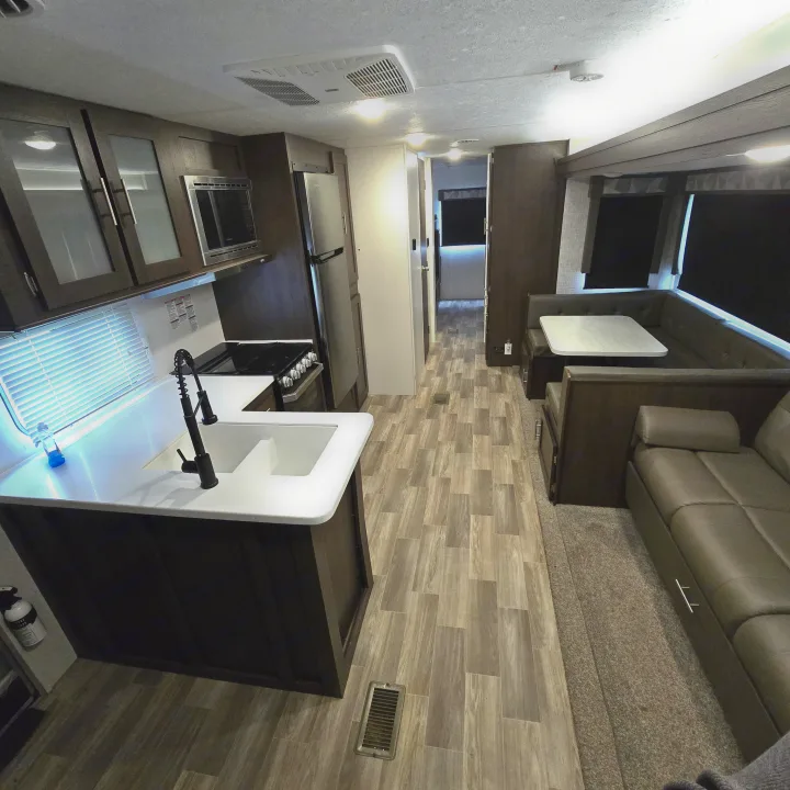 Inside a modern RV rental: full kitchen with sink/stove, dinette, and sofa. Wood-look flooring and ample living space.. Forest River Salem 2019