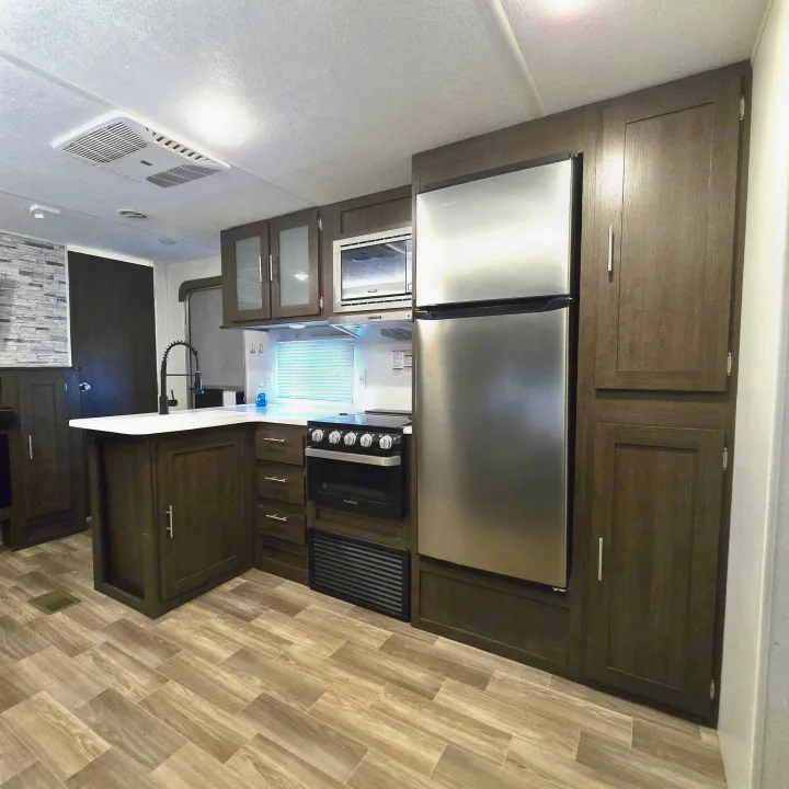 Modern RV rental kitchen featuring dark wood cabinets, stainless steel appliances, an island sink, and wood-look flooring.. Forest River Salem 2019
