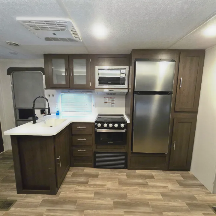 Modern RV rental kitchen features dark cabinets, white counters, stainless steel appliances, and a wood-look floor.. Forest River Salem 2019